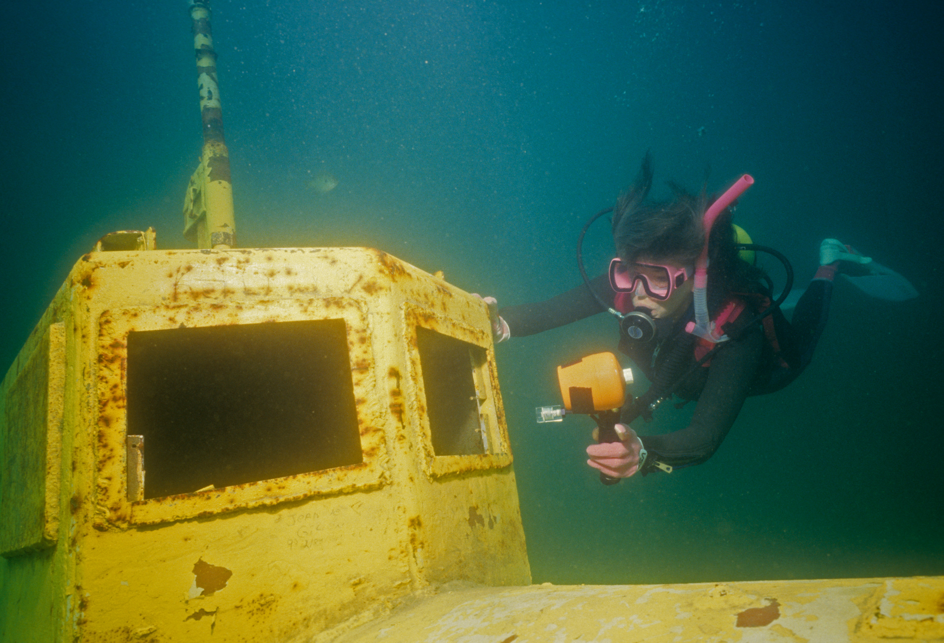 Female diver uses her dive light to inspect the interior surfaces of a WWII U-boat; the yellow submarine is just one of the many sunken attractions that can be found at Illinois&#039;s Pearl Lake.