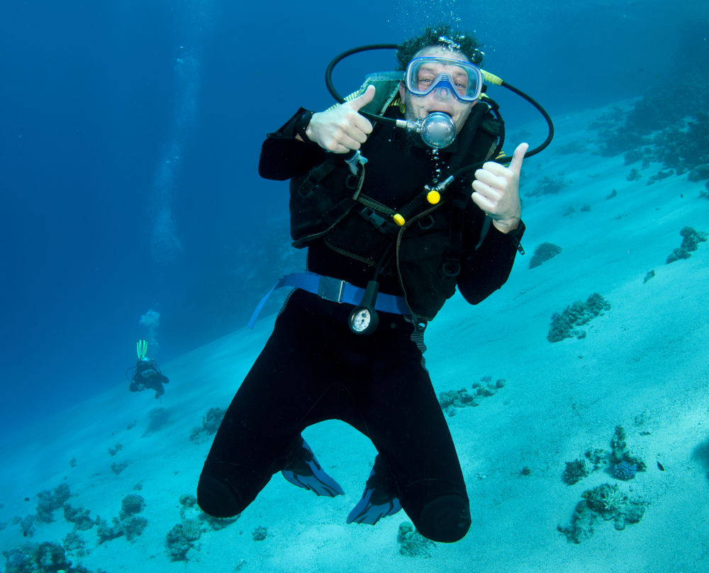 Male diver uses the ascend scuba hand signal to tell his dive buddy he is ready to ascend to the surface