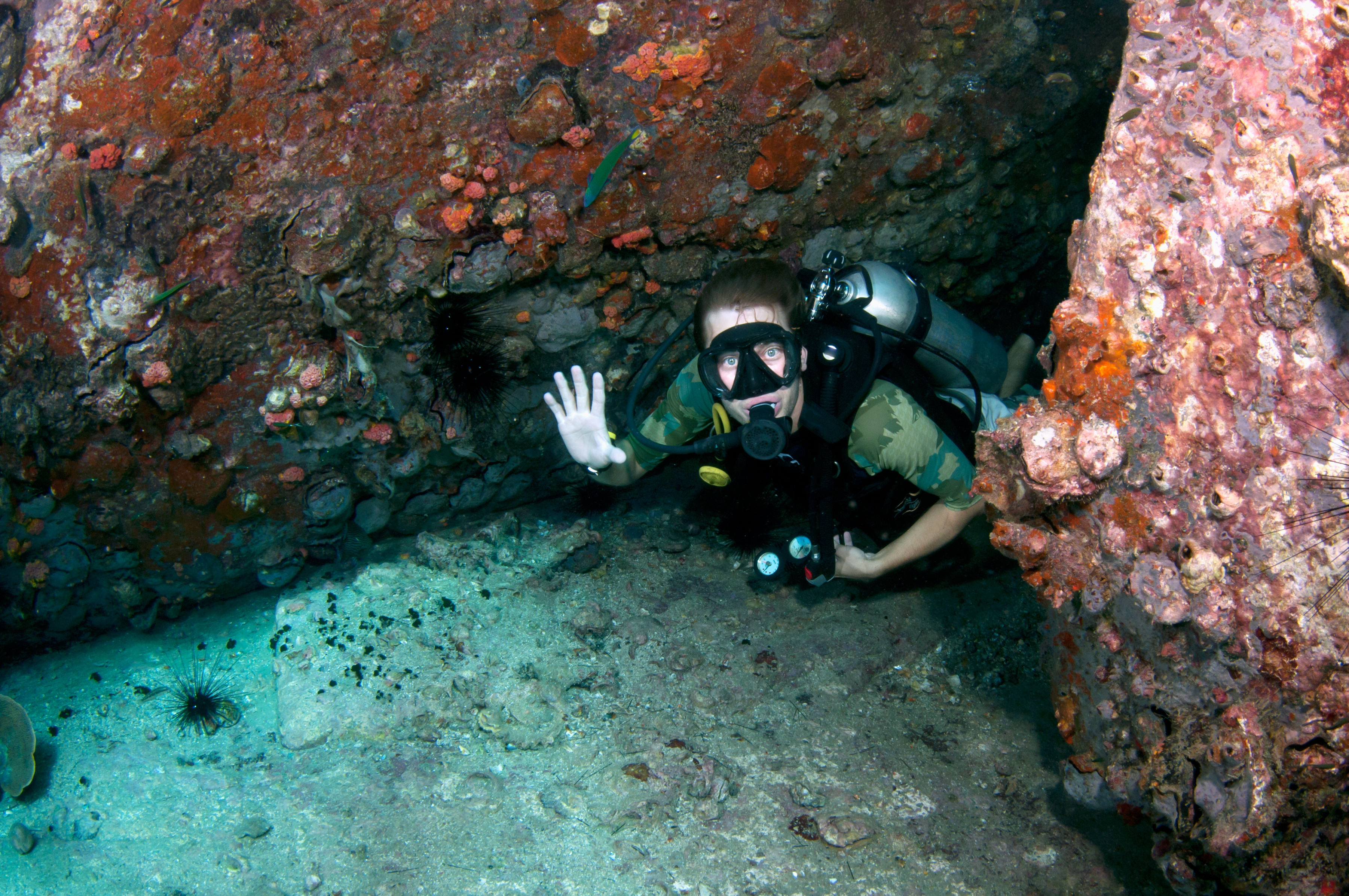 Male diver uses the hold on scuba hand signal to stop fellow divers from entering a cave with a small opening