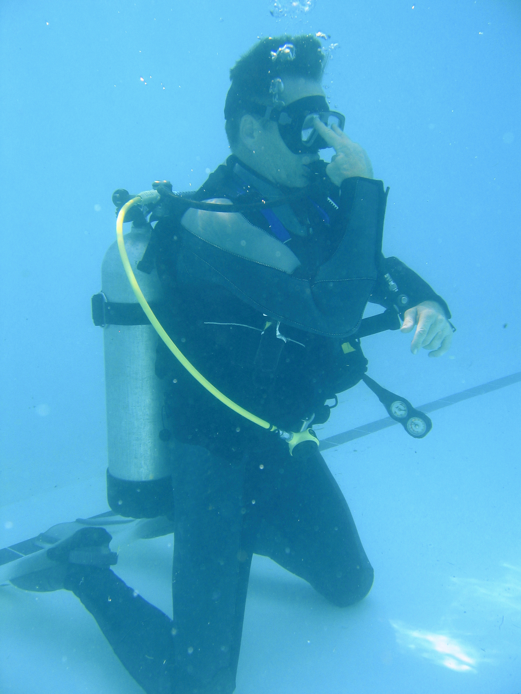 Scuba instructor utilizes the look scuba hand signal to capture the attention of his dive students in a pool environment