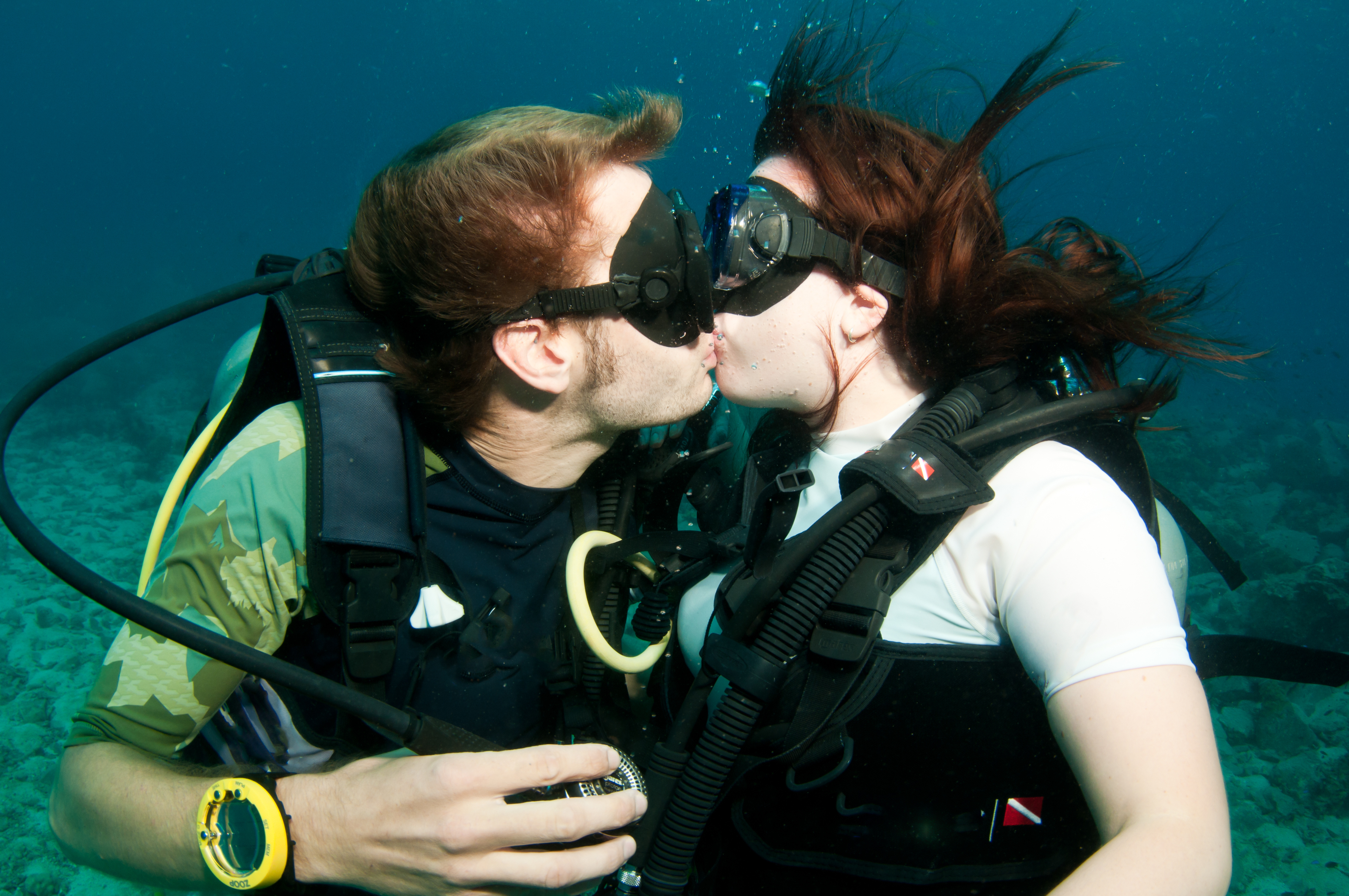 man and woman divers embrace eachother with and underwater kiss