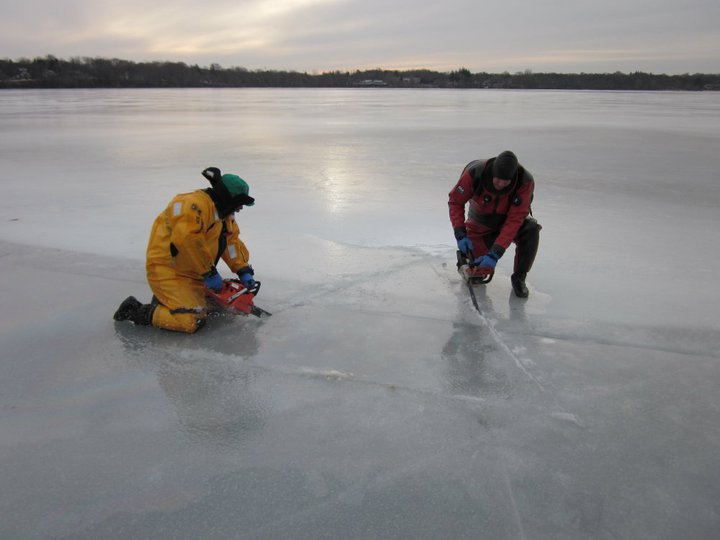 Two divers use chainsaws to cut a hole in the ice for diving