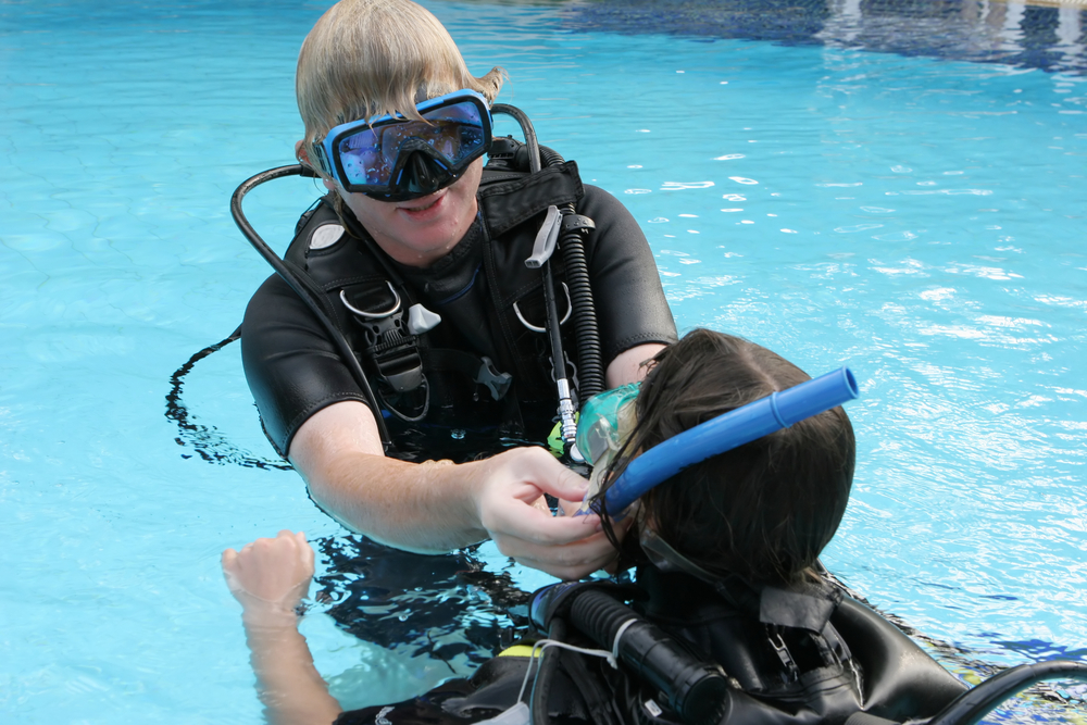 Dive instructor helps student with his mask before beginning underwater skills practice