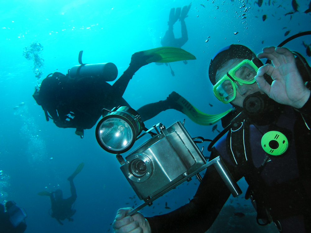 Underwater photographer signals ok while holding his camera equipment