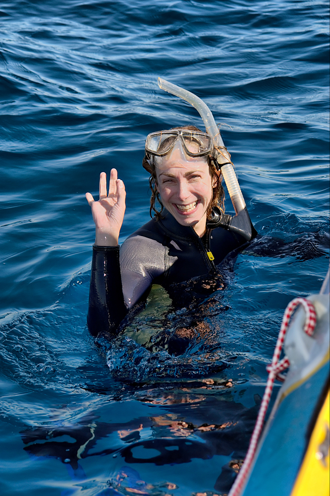Female diver waving hello as she makes her way towards the boat ladder