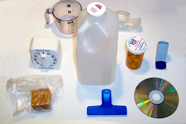 A variety of household plastics including juice container, prescription container, plastic clip, measuring cup, timer and more