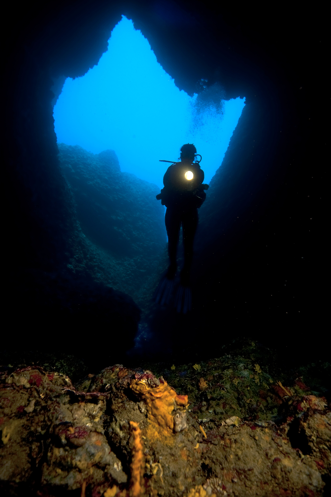 Cave diver shines his dive light into an underwater cavern as he enters it from the open water