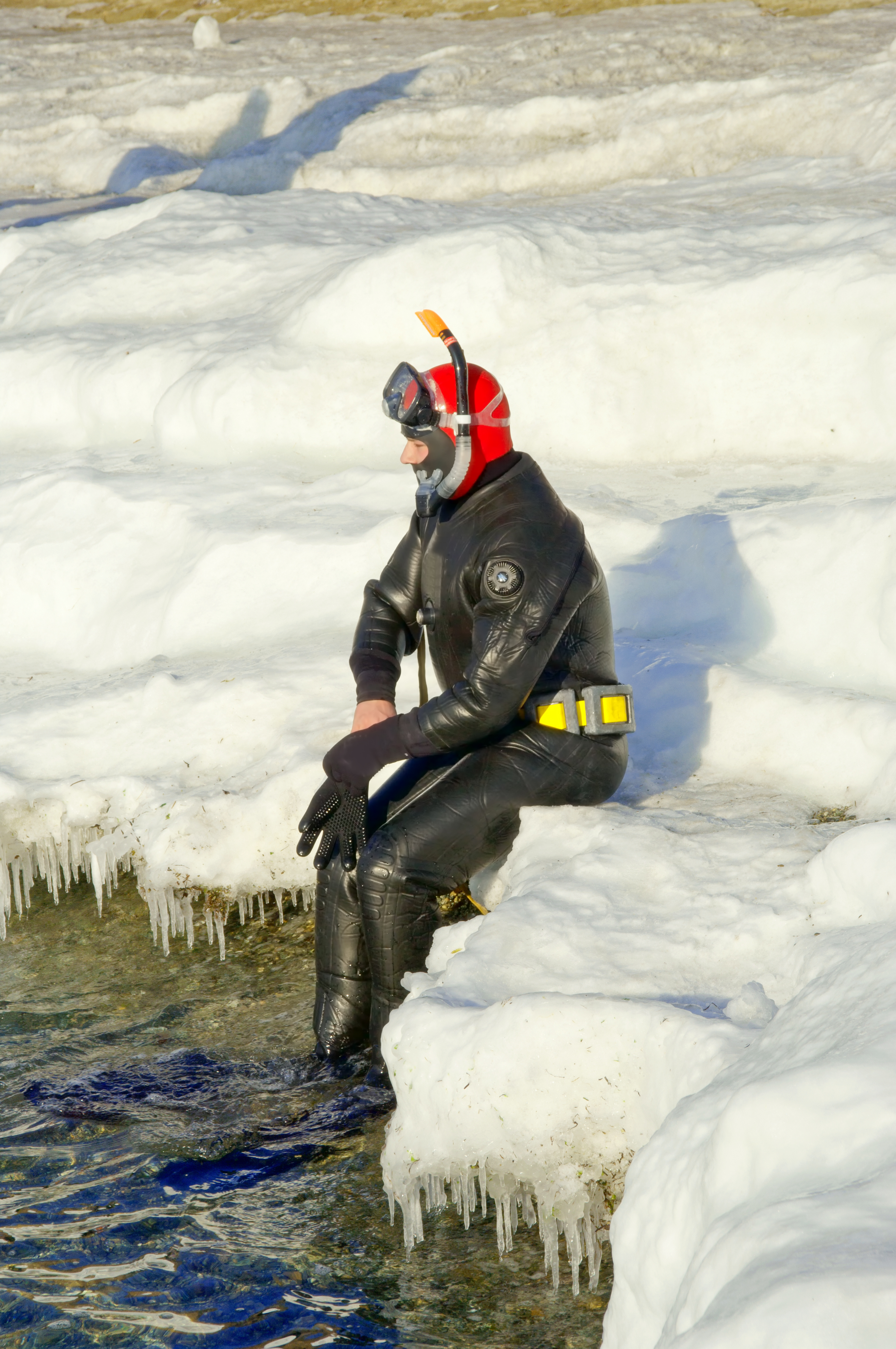 Male diver sits comfortably on the edge of the ice after a dive knowing that he packed the proper clothing and dive gear to ensure that his trip is enjoyable 