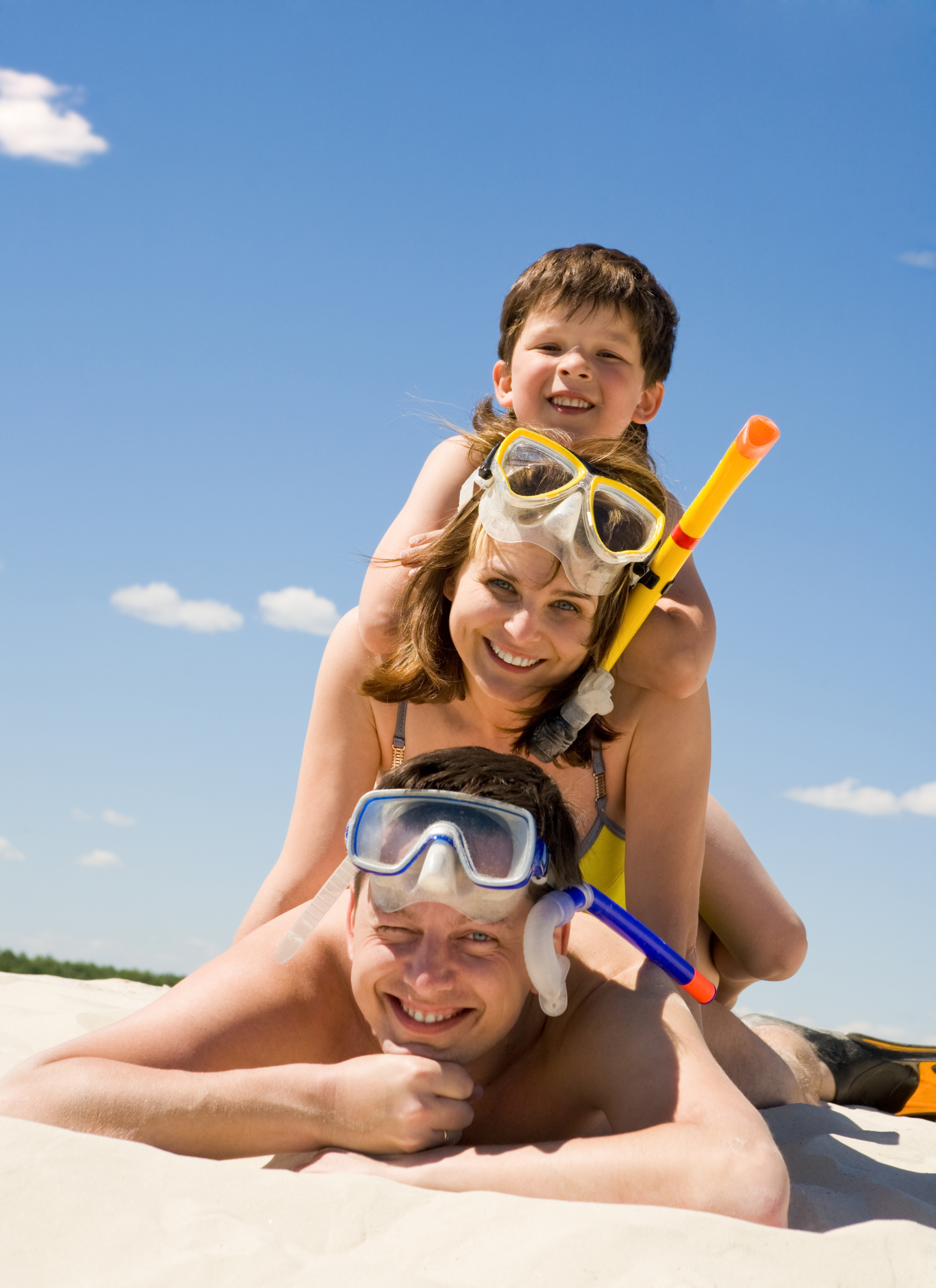 Father, mother, and child lay stacked on top of each other with snorkel gear taking in the beach between dives
