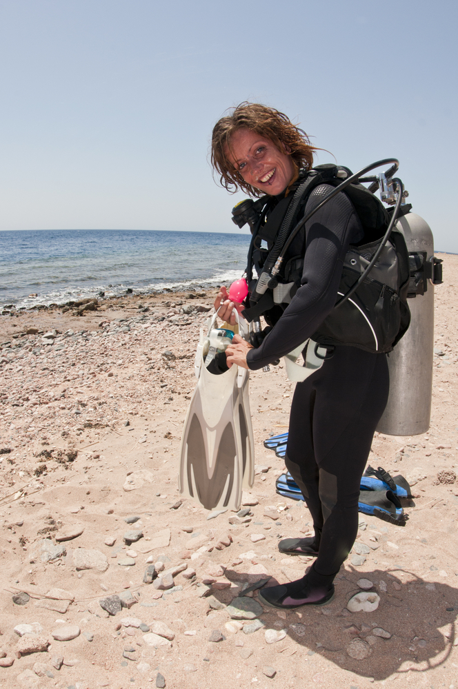 Female shore diver smiles at her dive buddy as she grabs her fins and heads out to the big blue ocean