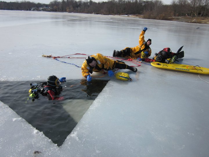 Several ice divers practice cutting a hole in the ice