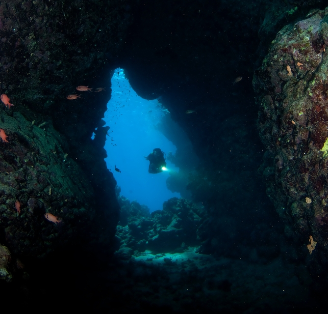 Cave diver carrying multiple light sources at the entrance to an underwater cave