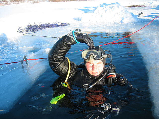 Young male ice diver signals OK before heading beneath the ice for an exploration dive