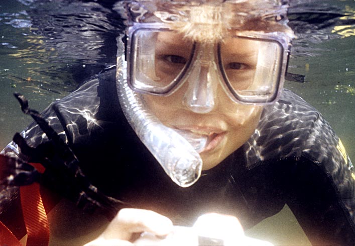 Child diver tests scuba snorkel with purge valve underwater ensuring his comfort and safety before his parents make the purchase