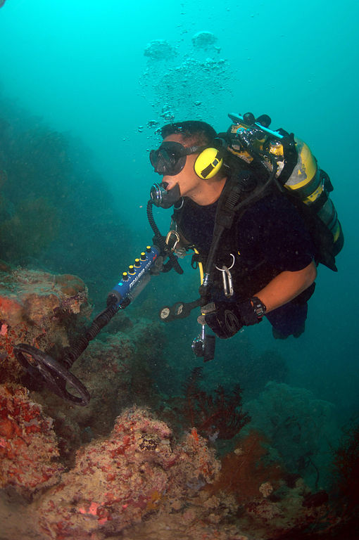 Male wreck diver uses underwater metal detector to search for sunken treasure