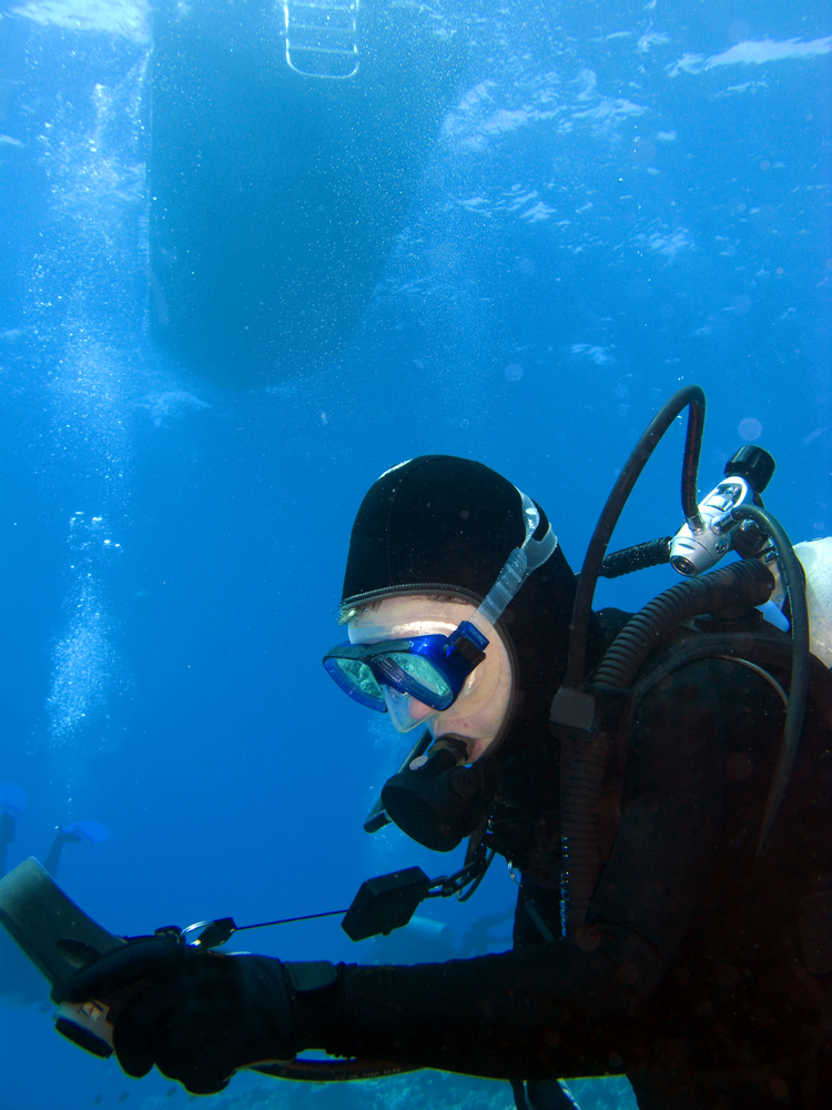 Male diver checks his depth, time, and air at safety stop before heading back towards the dive boat