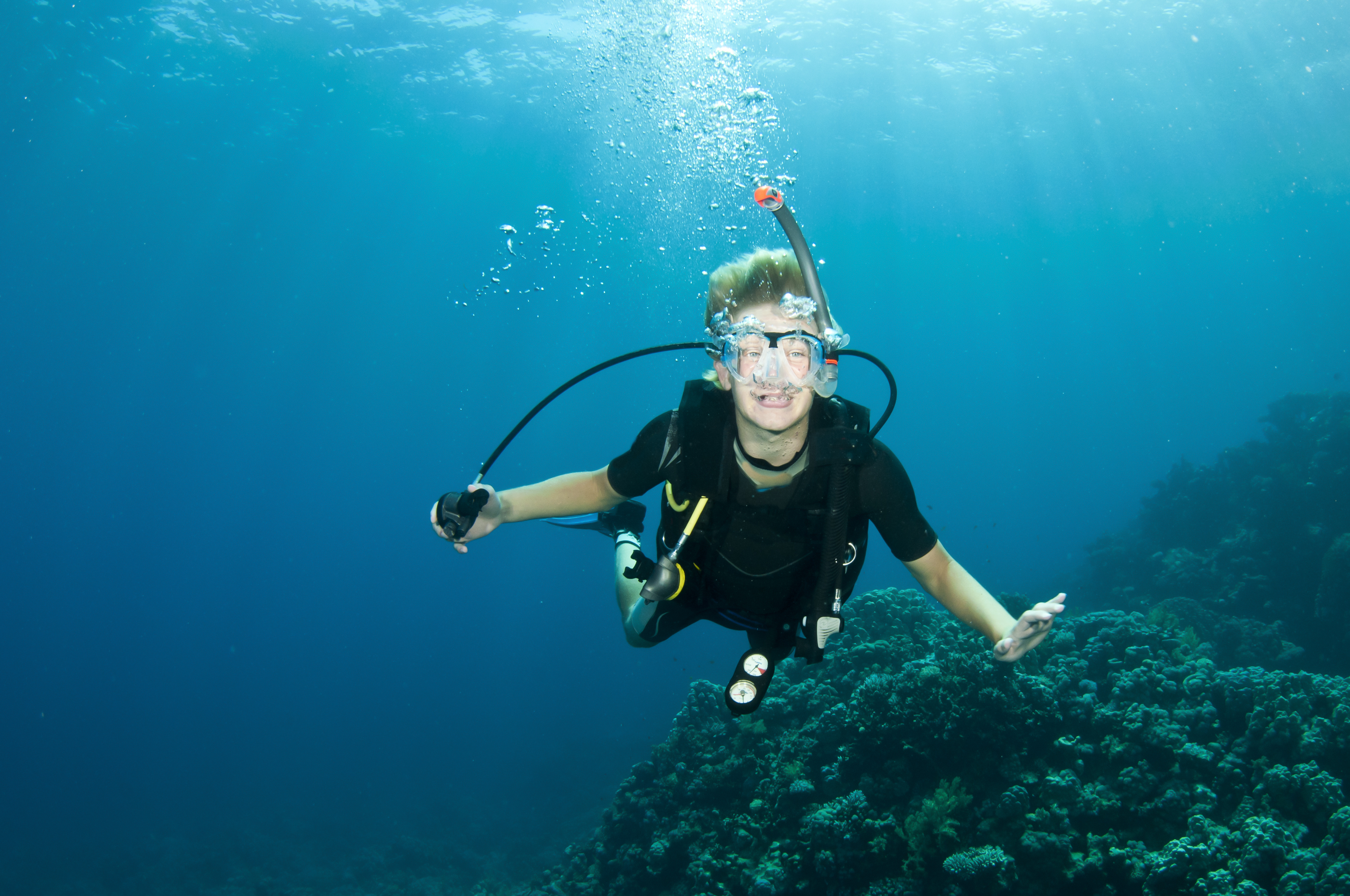 Inexperienced male diver suffering from nitrogen narcosis removes his regulator to smile and begin talking during a dive