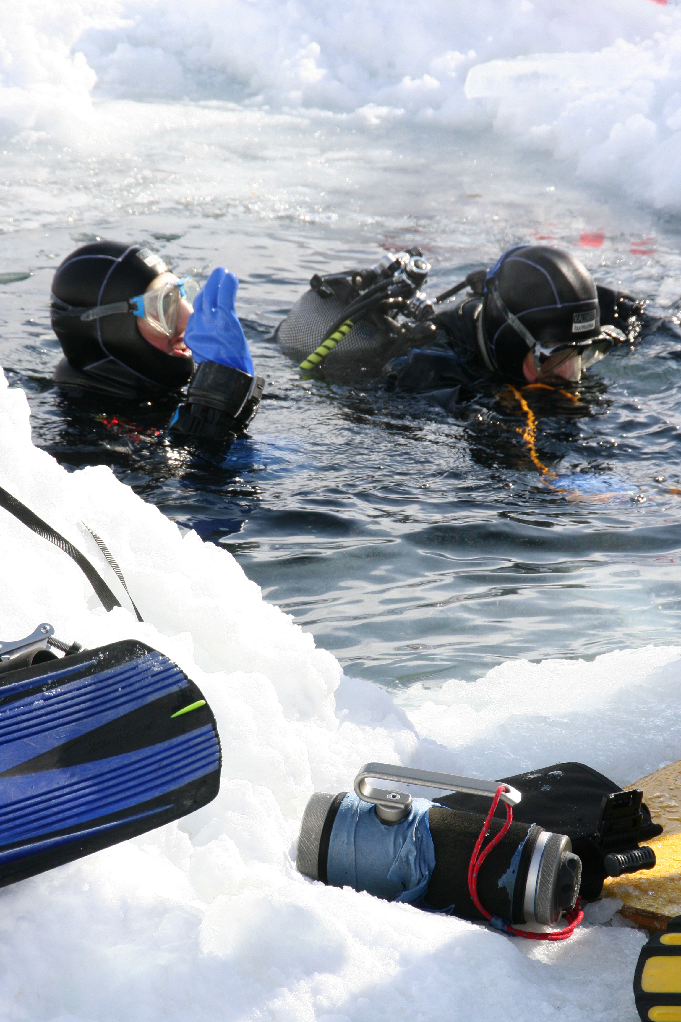 Team of ice divers with full gear signal they are OK before descending into the frigid waters