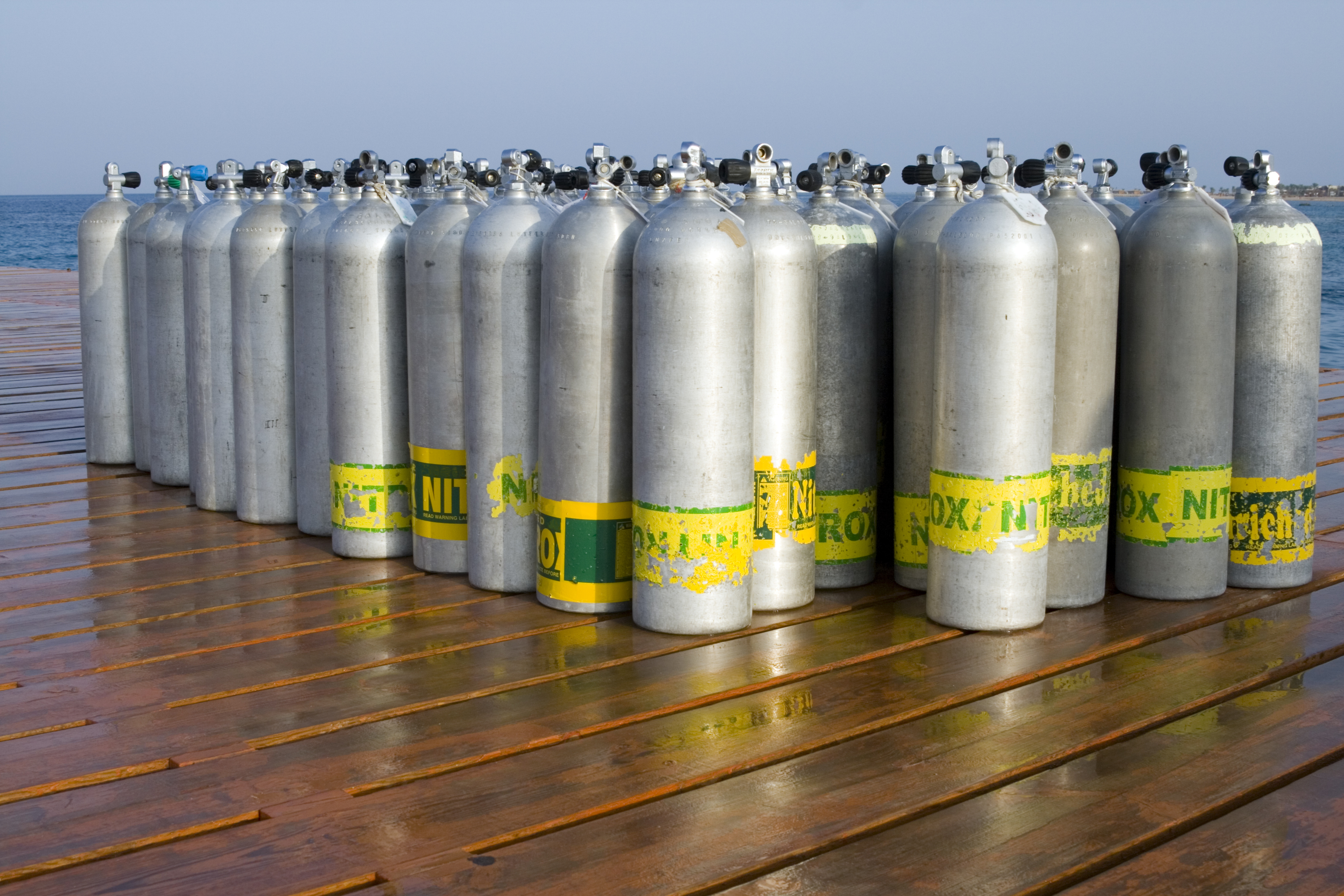 A collection of air, nitrox, and mixed gas scuba cylinders ready to be examined before being used by divers