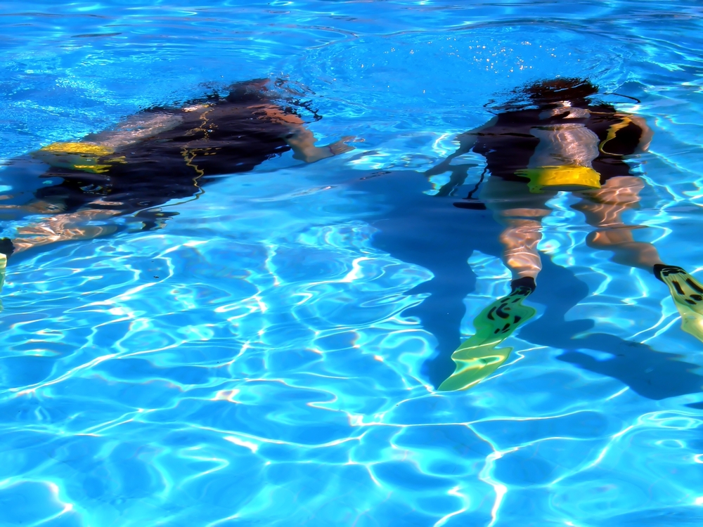 Male scuba diver under the supervision of his dive instructor practices clearing his mask at the bottom of the pool before heading out to complete an open water dive