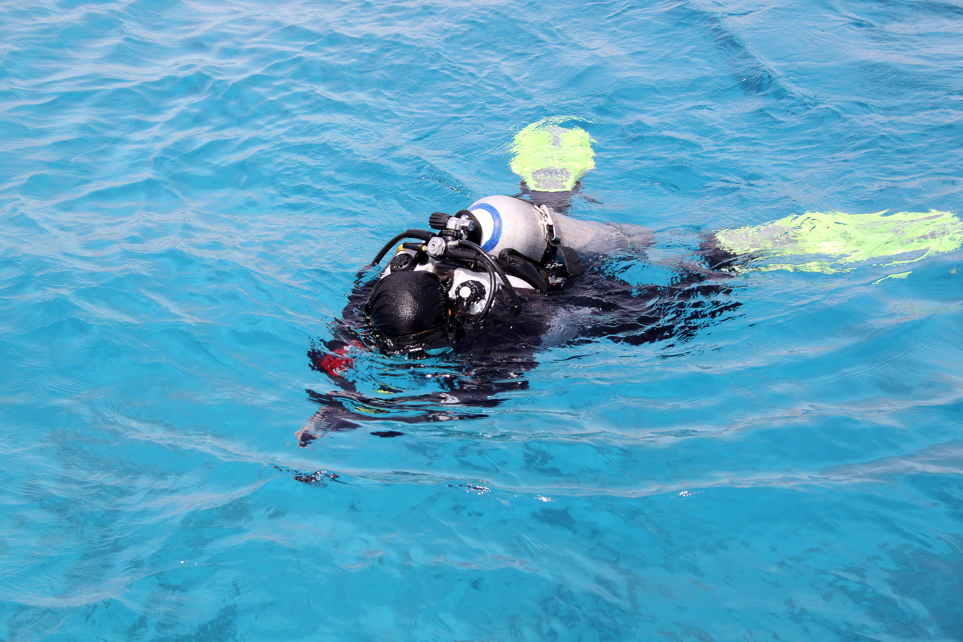 Scuba diver floating on the surface of the water face down before being rescued by a nearby diver