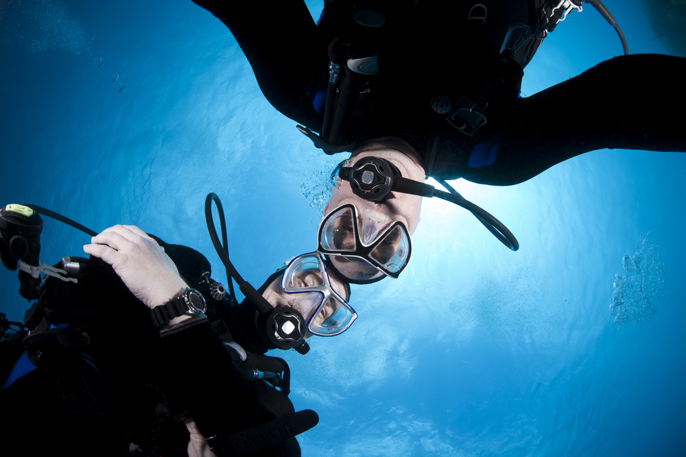 Two dive buddies touch heads and act responsibly throughout their dive in the Caribbean Sea avoiding a scuba diving accident and subsequent lawsuit