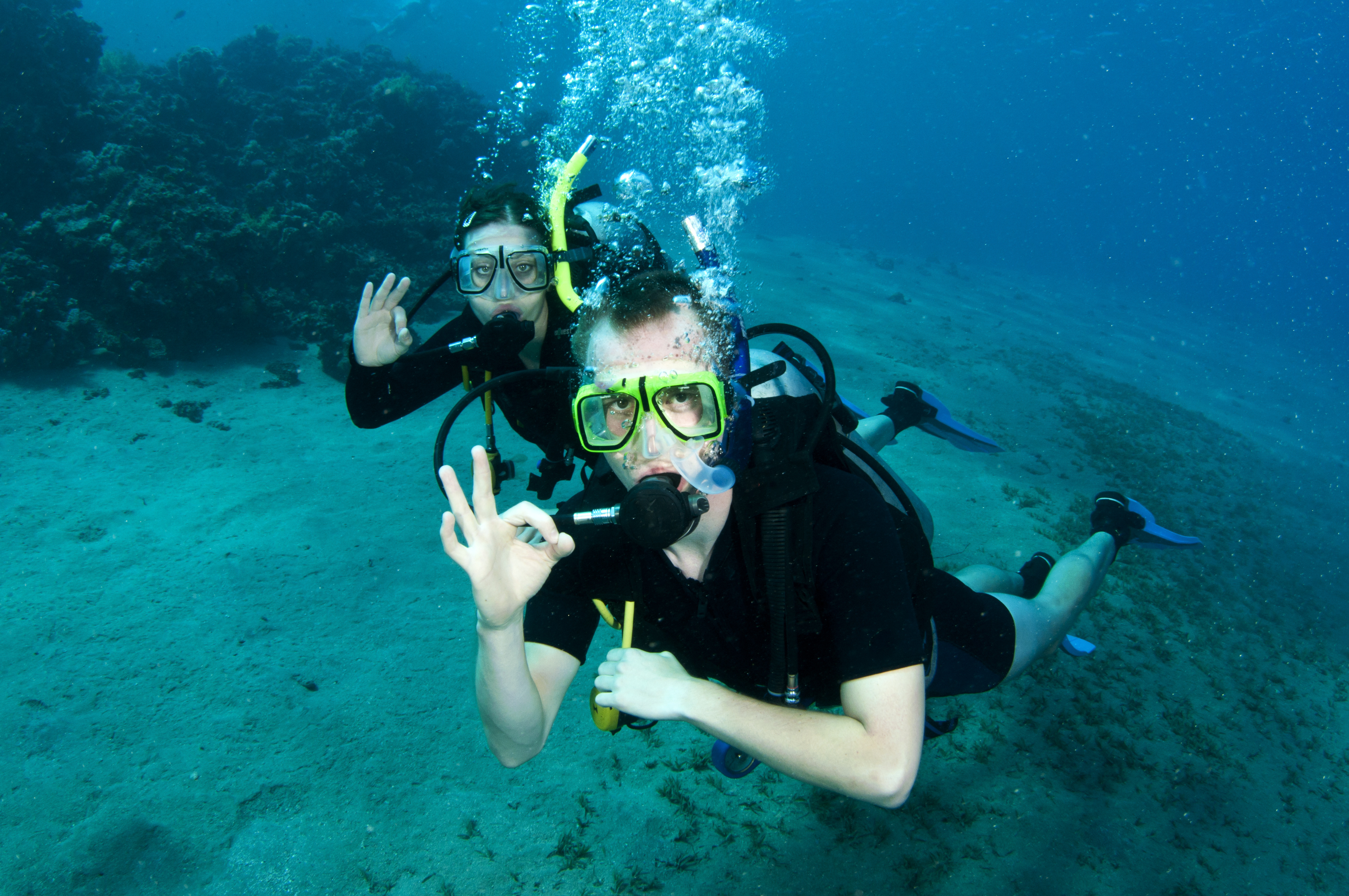 Two scuba divers avoid buddy separation by staying close to eachother and signal divemaster that they are ok