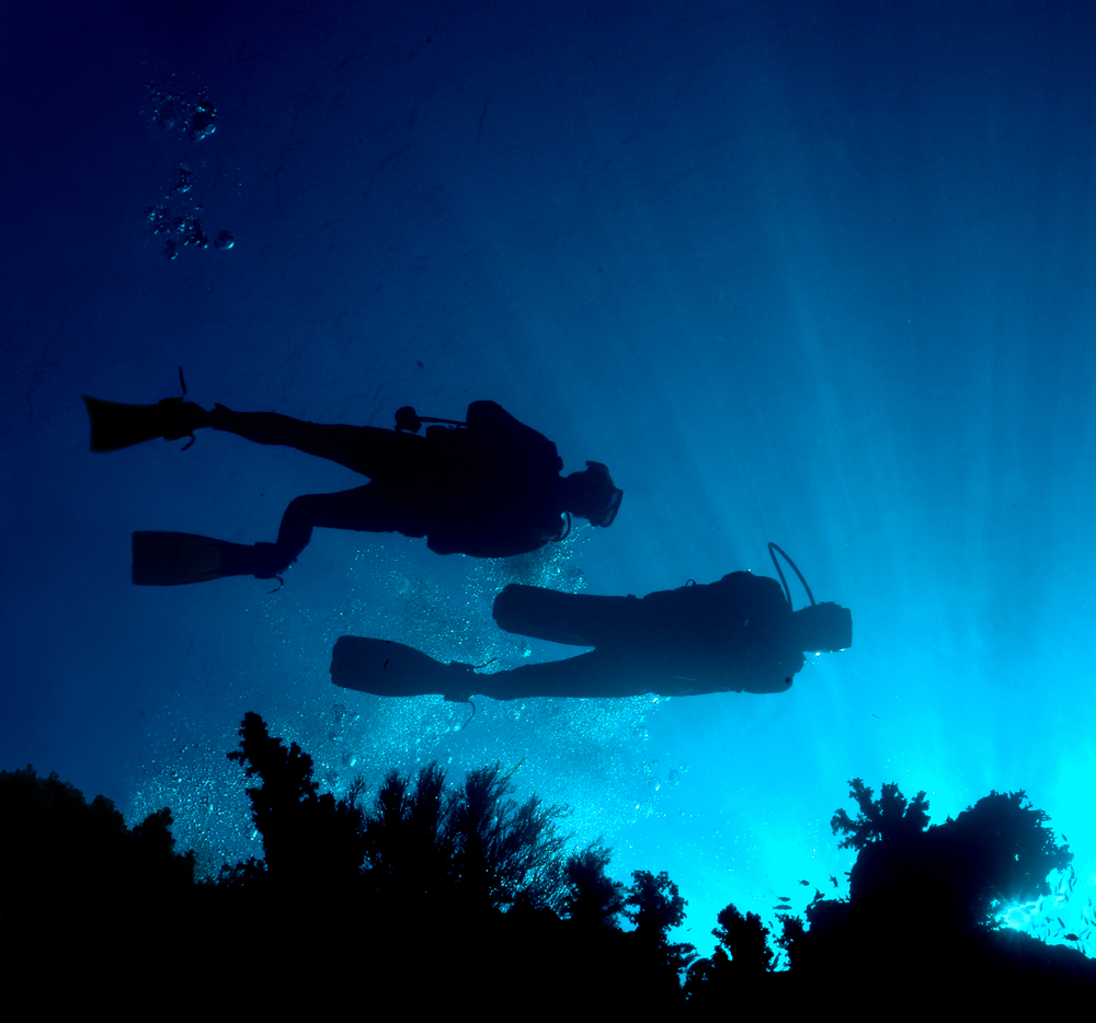 Underwater photographer shoots the silhouettes of two divers with sunlight in the background to help enhance the blues