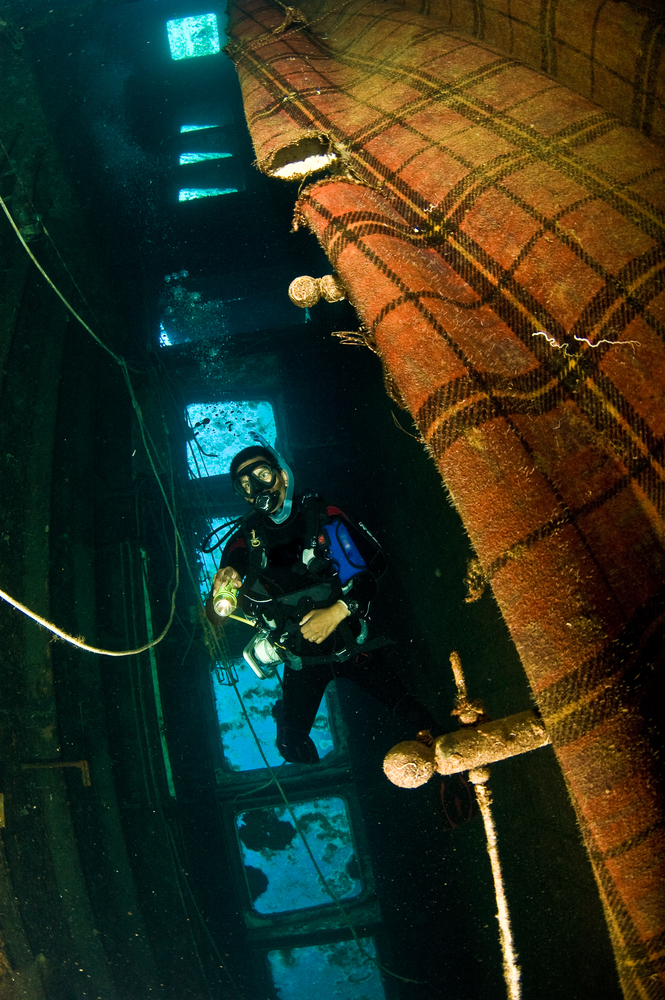 Wreck diver shining his dive light on the inside of the wreck being careful to avoid any entrapment hazards