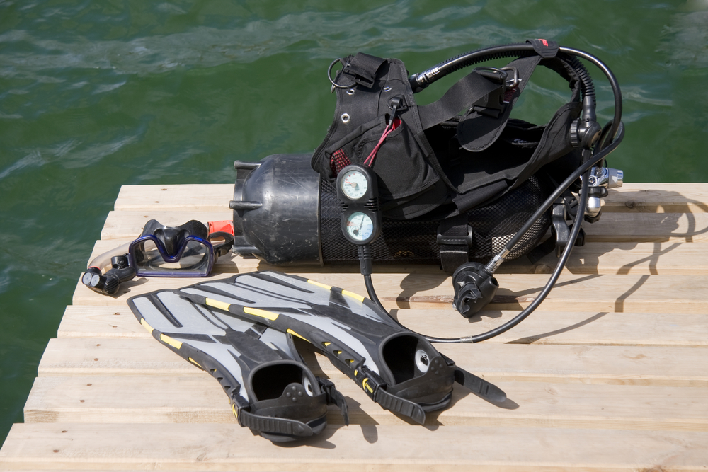 A set of used scuba gear, including dive tank, buoyancy compensator, regulator, mask, fins, and snorkel, lying on wooden dive platform