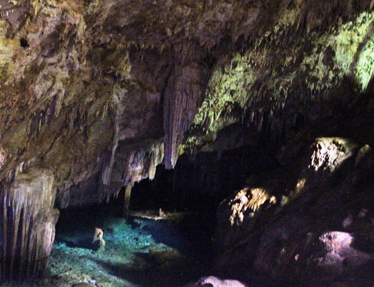 Crystal clear blue water runs through this limestone cave surrounded by huge boulders