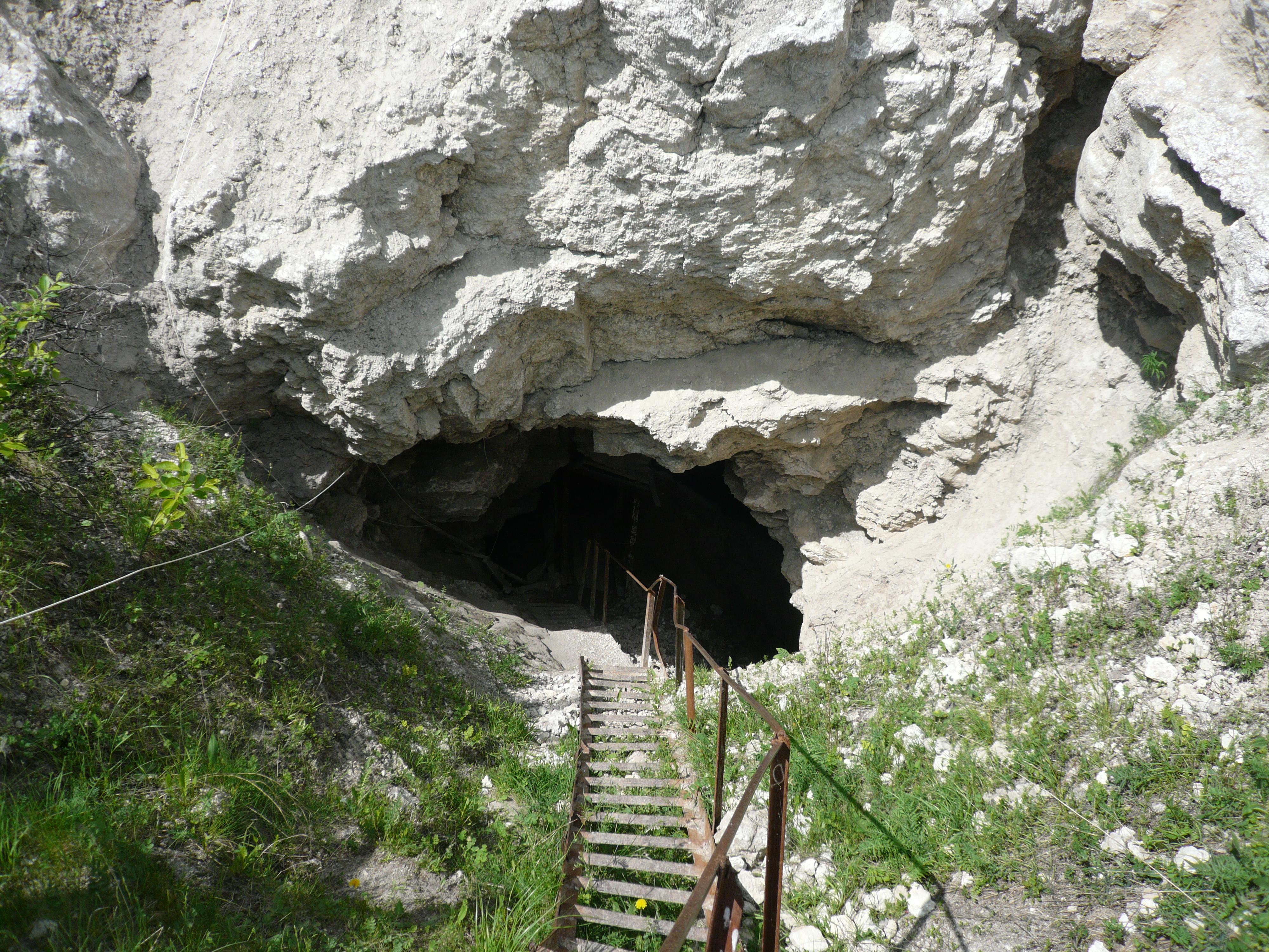 A series of wooden steps lay across a grassy area that slopes towards the entrance to Russia's Ordinskaya Cave, also known as Orda Cave