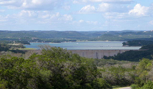 Medina Lake in Texas with the dam walls in the forefront and lush mountainous terrain in the backdrop