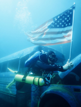 Male diver holds the american flag as he makes his way past a sunken bus at the bottom of Lake Rawlings in Virginia