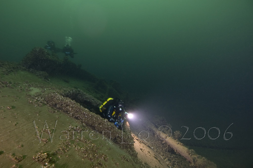 Several divers exploring the Tiller Wreck in Lake Ontario with one diver exiting with his dive light from a hole in the wreck