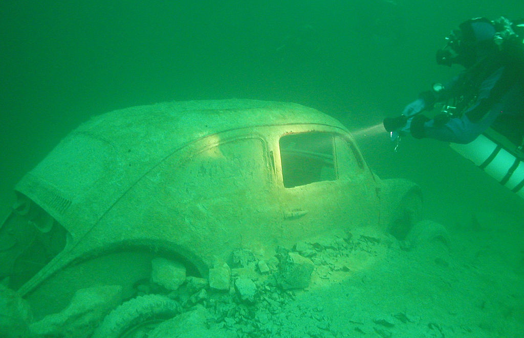 Male diver shines his dive light at an old Volkswagen Beetle found at the bottom of Germany&#039;s Lake Walchensee
