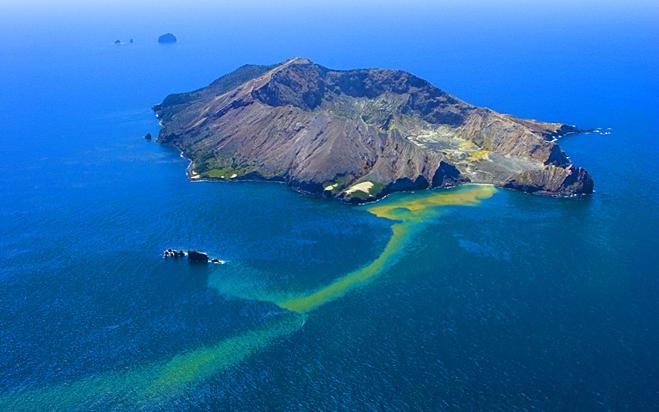 Aerial view of White Island in New Zealand showing a stream of sulphur from the live volcano entering the water surrounding the island