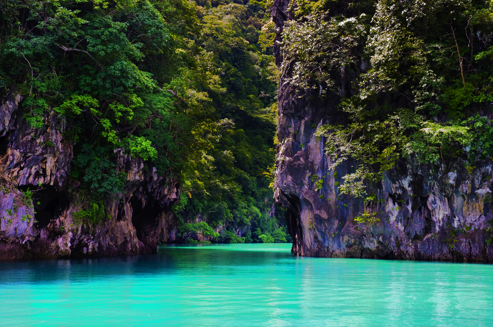Towering boulders covered in lush greenery create passageways for the crystal clear blue water to flow on the island of Thailand